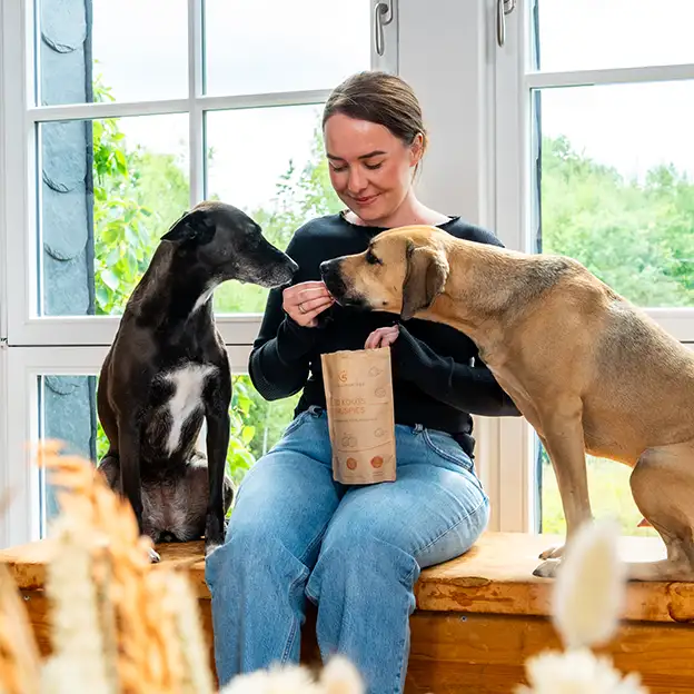 Tierhalterin gibt zwei Hunden einen Snack und hält eine Packung BIO KOKOS KNUSPIES.