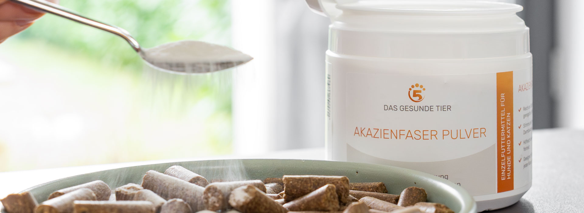 Ergänzungsfuttermittel „Gelenk Support“ von Das Gesunde Tier auf einem Waldweg, im Hintergrund ein sitzender Hund zwischen Wiesen und Bäumen bei Tageslicht.