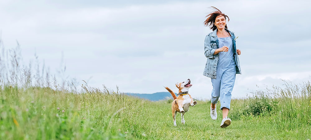 Frau läuft mit Beagle über die Wiese und freut sich