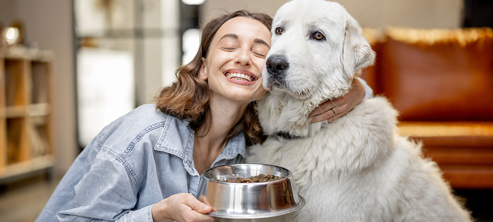 Lächelnde Frau mit Futternapf und weißem Hund
