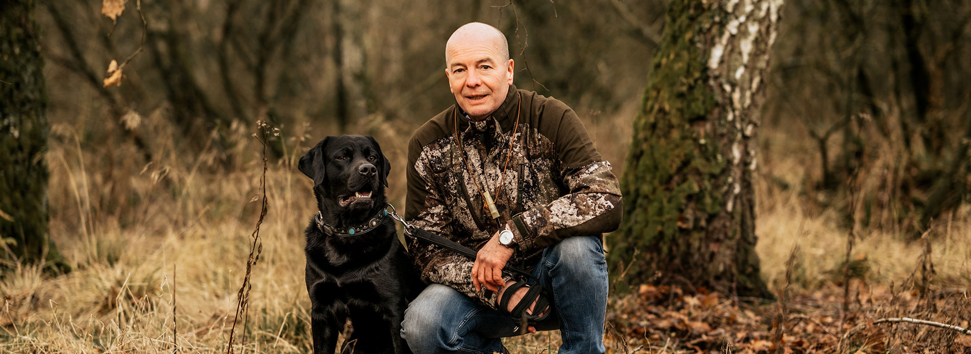 Tierarzt Thomas Backhaus hockt im Freien neben einem schwarzen Hund und blickt in die Kamera.