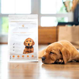 Schlafender Welpe neben einer Packung SUNNY Welpenfutter von Das Gesunde Tier.