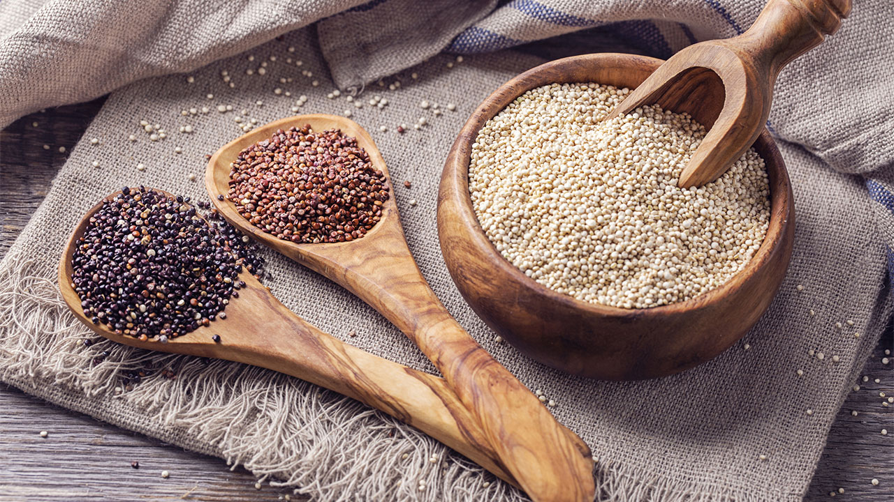 Quinoa- und Chia-Samen Liegen getrennt in einer Schussel und auf zwei Löffeln aus Holz.